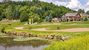 A golf course with a pond, a clubhouse, and surrounding trees.