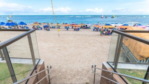 Una playa con una escalera que baja a la arena, rodeada de sombrillas y sillas de playa.