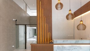 Una moderna área de recepción con un mostrador de madera, una puerta de cristal y luminarias colgantes.