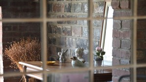 Ein rustikales Interieur mit einer Backsteinwand, einem Holztisch mit einer Vase getrockneter Pflanzen und einer Hasenstatue.