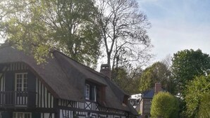 Ein traditionelles Fachwerkhäuschen mit einem Strohdach, einem weißen Zaun und einem Weg zu einem Steinhaus.