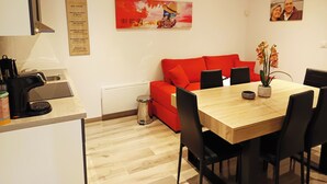A modern kitchen with a coffee machine, a dining table with chairs, a red sofa, and a painting on the wall.