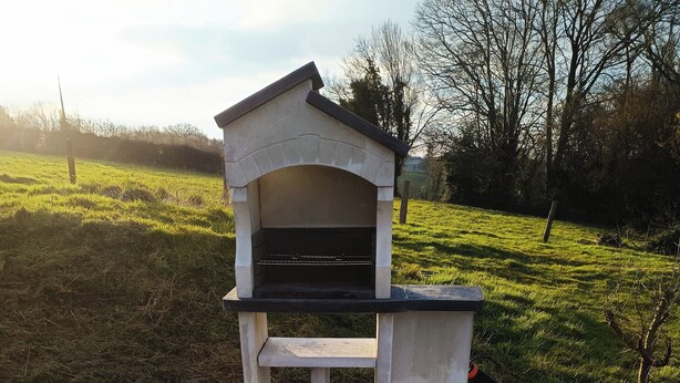 A stone barbecue grill with a bench, set on a tiled patio.