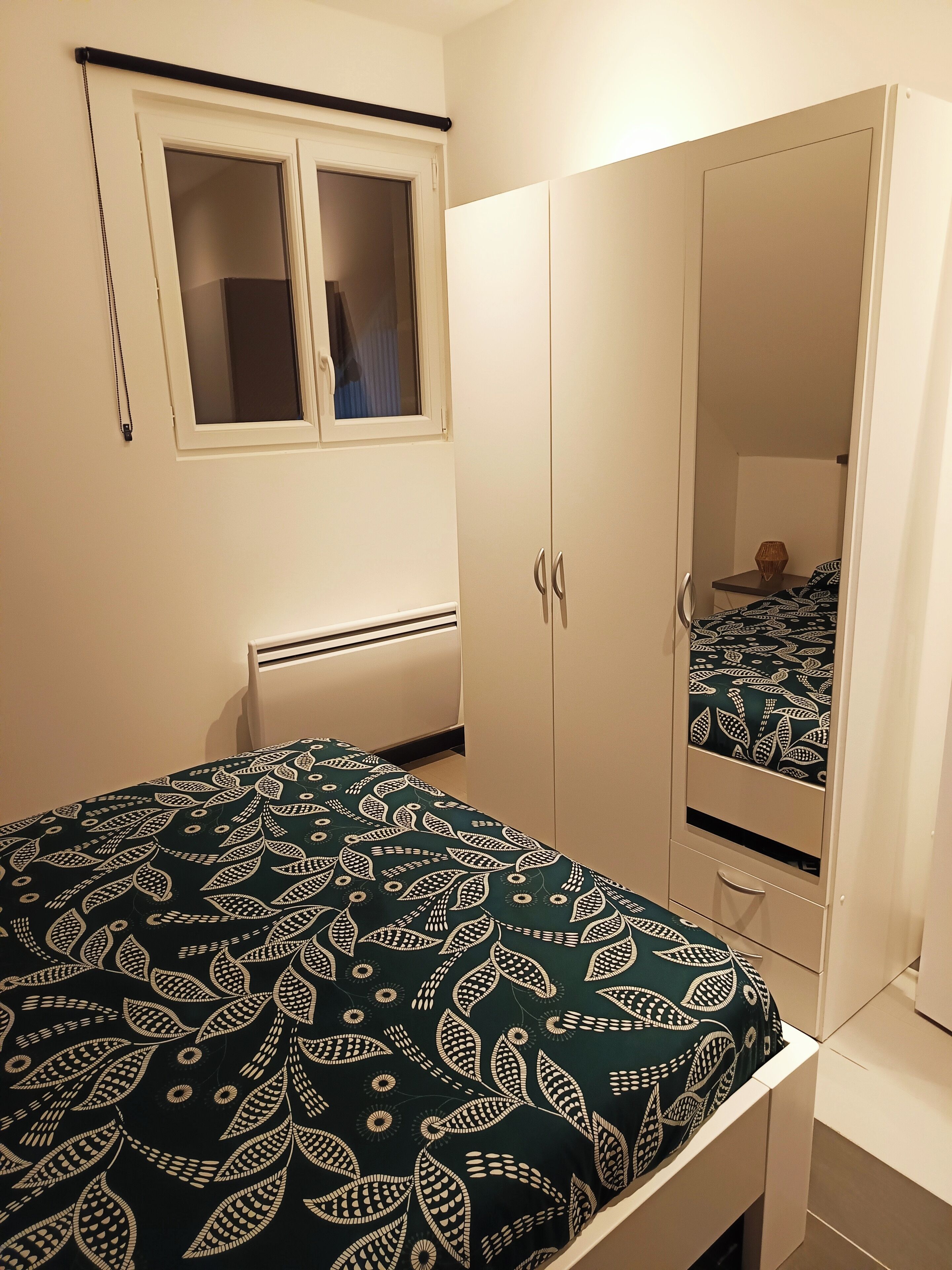 Quarto com cama, guarda-roupa, janela e radiador.