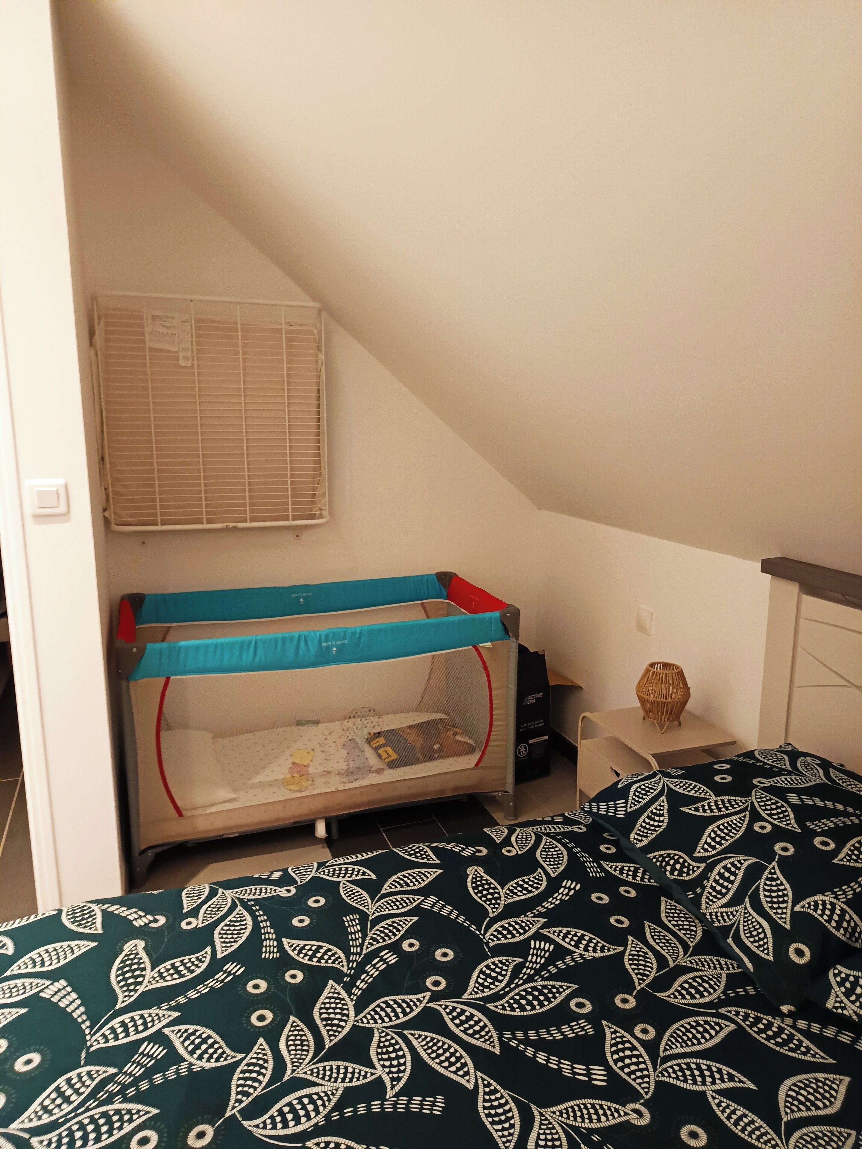 Une chambre avec un lit superposé, une petite table de chevet avec une lampe et une fenêtre avec des stores.