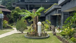 Un edificio moderno con techo plano, rodeado de un jardín bien cuidado con diversas plantas y un macetero circular central.