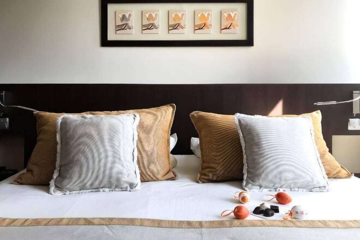 A neatly made bed with four pillows, a framed artwork above, and a tray with snacks on the bed.