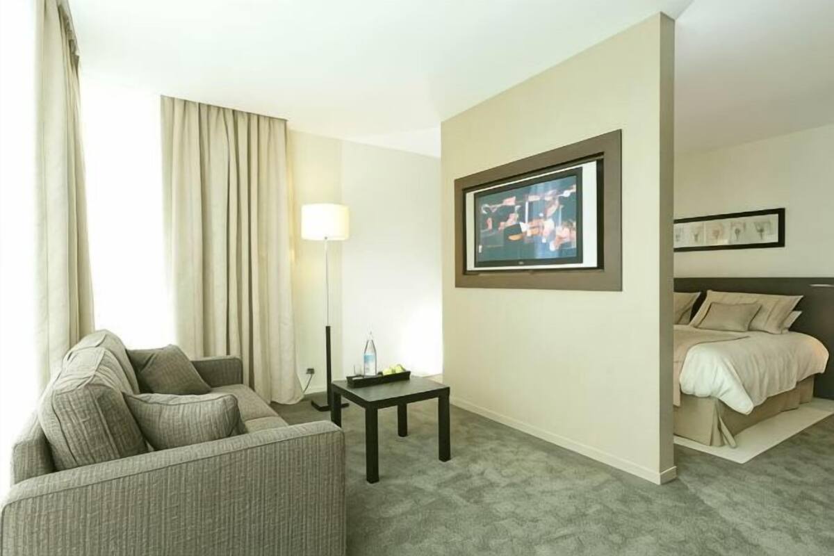 A hotel room with a bed, a sofa, a small table, a lamp, and a framed picture on the wall.