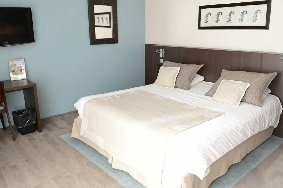 A neatly made bed with pillows, a bedside table with a lamp, and a framed picture on the wall.