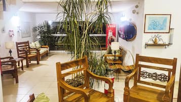 Een kamer met houten meubels, waaronder stoelen en een bank, een grote potplant en een spiegel aan de muur.