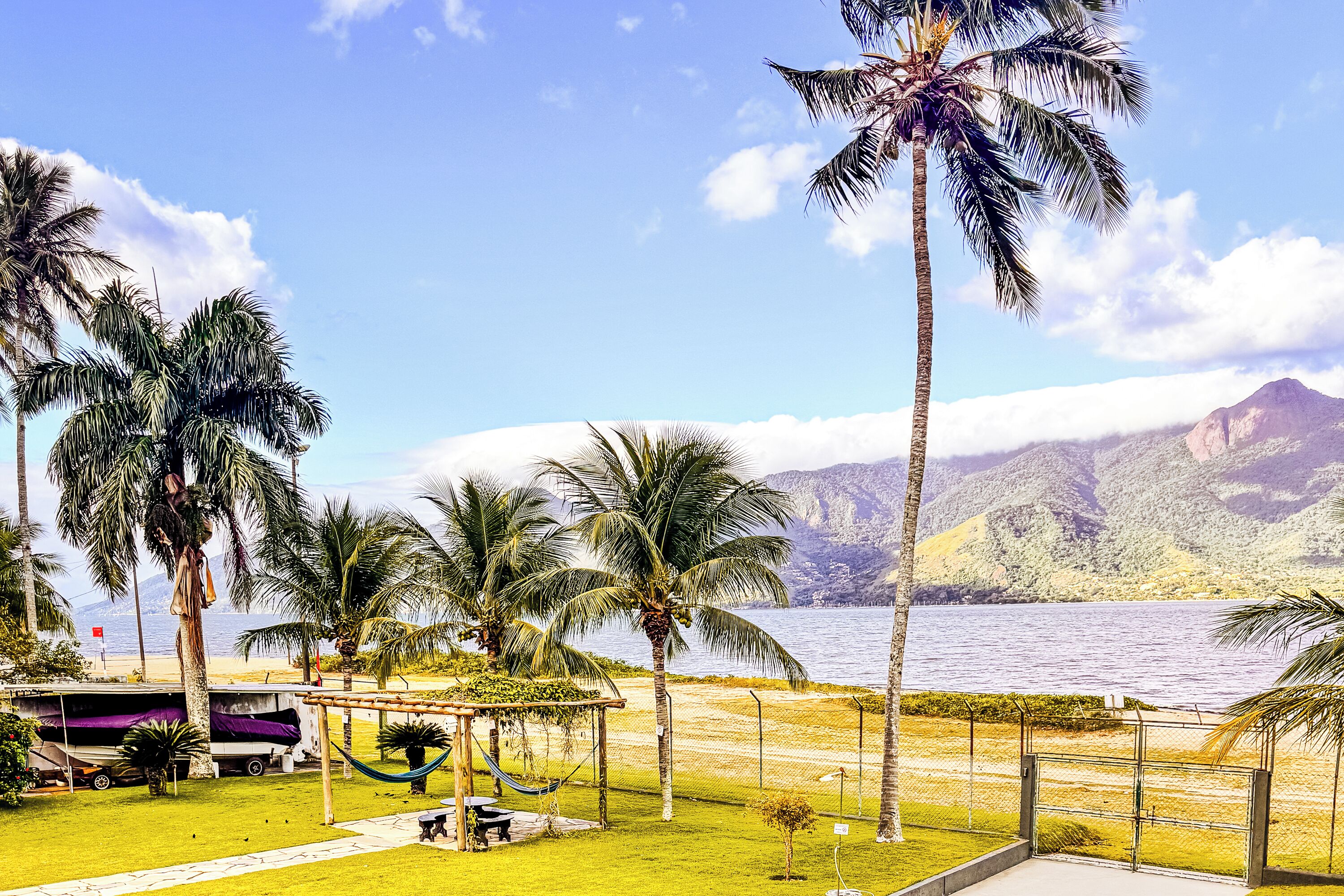 A tropical resort with palm trees, a hammock, and a view of the ocean and mountains.