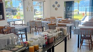 A restaurant with multiple tables and chairs, a buffet counter with food items, and large windows offering a view of the outdoors. - VELINN Hotel Guarda Mor (São Sebastião)