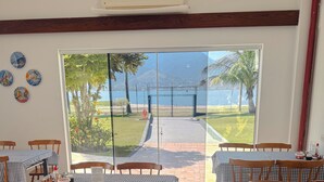 A dining area with checkered tablecloths, wooden chairs, and a view of a garden and water body through large glass doors. - VELINN Hotel Guarda Mor (São Sebastião)