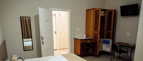 A hotel room with a bed, a desk, a wardrobe, a television, and a bathroom door.