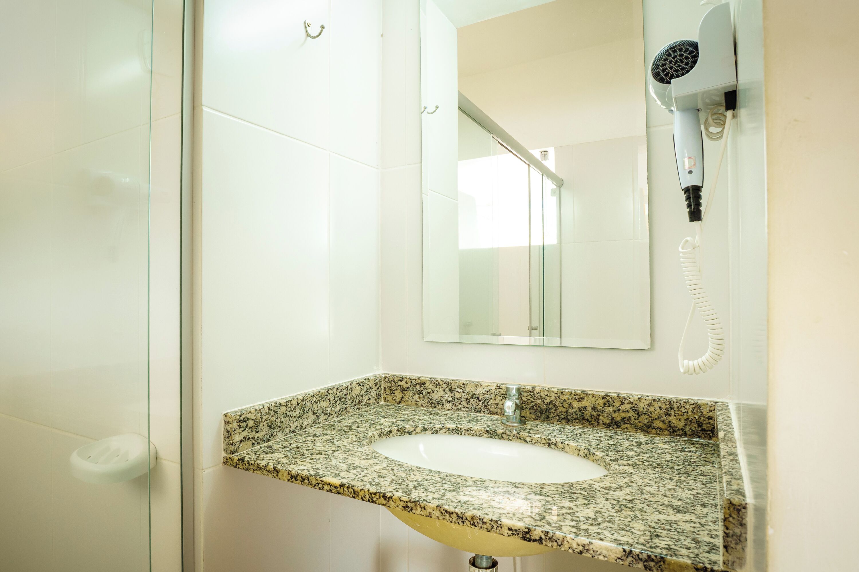 A bathroom with a granite countertop sink, a mirror, and a hairdryer mounted on the wall.