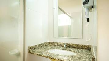 A bathroom with a granite countertop sink, a mirror, and a hairdryer mounted on the wall.
