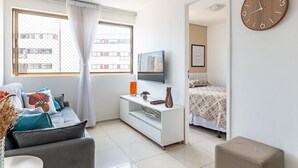A modern living room with a sofa, TV, and a large clock on the wall. - 109 Flat completo e acolhedor nas Graças (Recife)