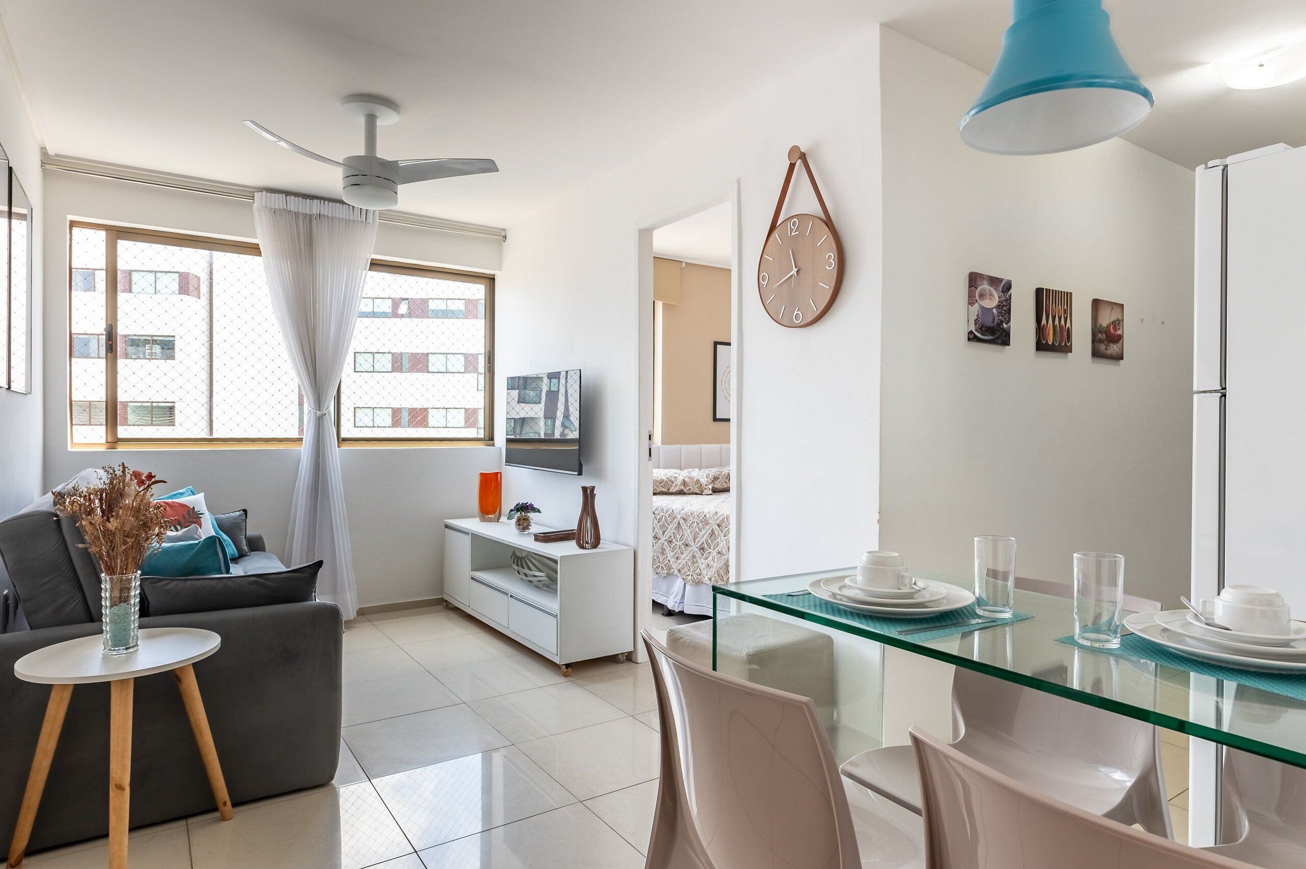 Un salon moderne avec un canapé, une table à manger en verre, un ventilateur de plafond et une horloge murale.