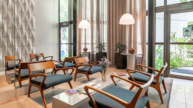 A modern lobby with wooden chairs, a central table, and large windows. - 109 Flat completo e acolhedor nas Graças (Recife)