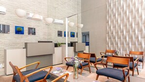 A reception area with a modern design, featuring a reception desk, several wooden chairs with blue cushions, and a decorative vase with flowers. - 109 Flat completo e acolhedor nas Graças (Recife)