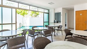 A modern indoor dining area with wicker chairs and round tables, large windows with a view of greenery, and a sign reading "Gracias." - 109 Flat completo e acolhedor nas Graças (Recife)