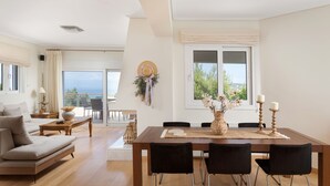 A spacious living area with a sofa, a dining table with chairs, and a balcony with a view of the sea. - Hegemoni Villa Porto Heli (Ermionida)