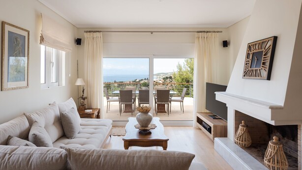 A spacious living room with a sofa, a coffee table, and a TV. There is a balcony with a view of the sea and a fireplace with decorative items. - Hegemoni Villa Porto Heli (Ermionida)