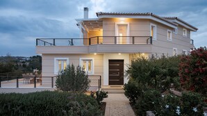 A modern two-story house with a balcony, a stone pathway, and surrounding greenery. - Hegemoni Villa Porto Heli (Ermionida)