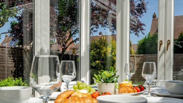 Ein Essbereich im Freien mit einem Tisch, der für ein Frühstück gedeckt ist, darunter Croissants, Trauben, Erdbeeren und Weingläser.