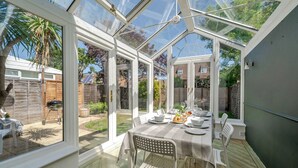 Ein Wintergarten mit Glasdach, einem Esstisch für vier Personen und Blick auf den Garten.