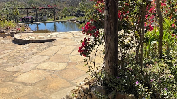 Un patio de piedra con cubierta de madera, una piscina y vistas a un lago y colinas.