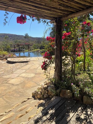 Um pátio de pedra com um deck de madeira, uma piscina e vista para um lago e colinas.