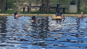 Una piscina con gente disfrutando el agua, rodeada de un paisaje natural y una montaña al fondo.