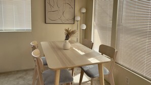 A dining area with a table, chairs, a vase with dried plants, and a wall-mounted abstract painting.