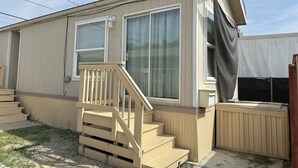 A single-story mobile home with a wooden deck and a small set of stairs leading to the entrance.