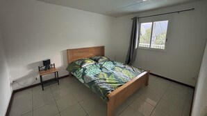 A bedroom with a bed, a small table, and a window with curtains. - O refuge d'Hell-Bourg (Salazie)