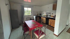 A compact kitchen with a dining area, featuring a table with chairs, a refrigerator, and a window with curtains. - O refuge d'Hell-Bourg (Salazie)
