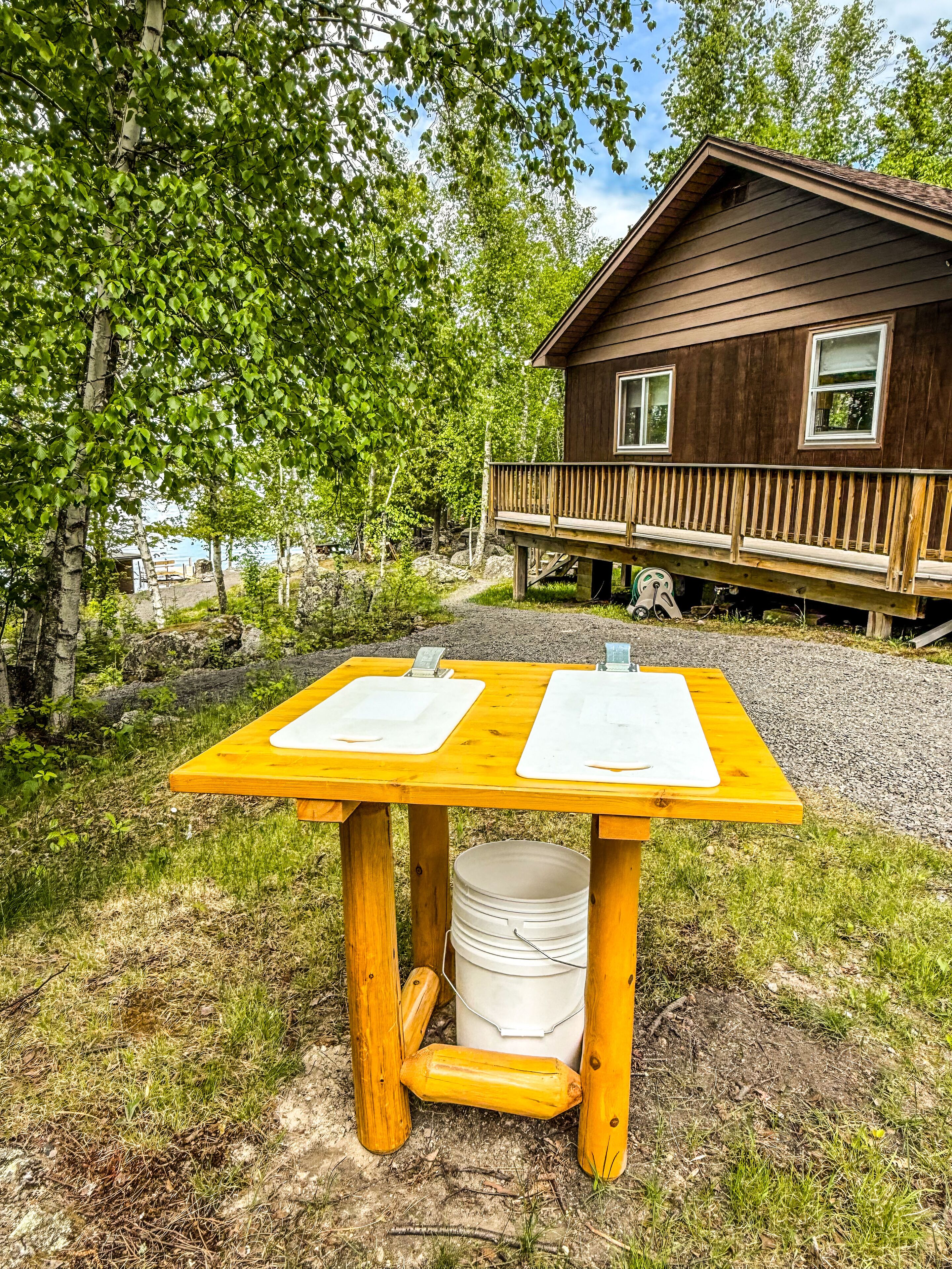 Une cabane en bois dotée d’une terrasse et d’une table sur laquelle reposent deux planches à découper blanches.