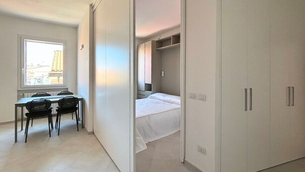 A bedroom with a bed, a closet, and a window with a view of buildings. - CN014 - Cesenatico, new three-room apartment on the canal port (Cesenatico)