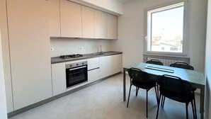 A modern kitchen with white cabinets, a gas stove, an oven, and a dining table with chairs. - CN014 - Cesenatico, new three-room apartment on the canal port (Cesenatico)