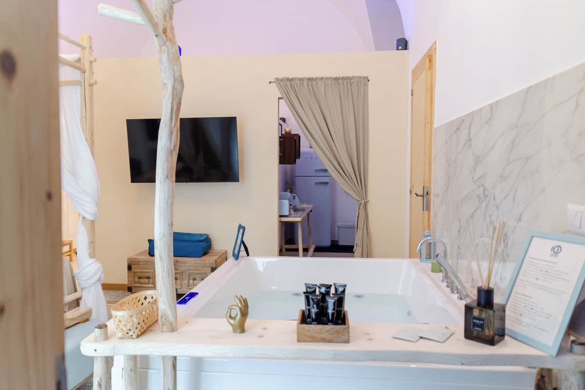 A modern bathroom with a bathtub, a wooden vanity, a television, and a marble wall.