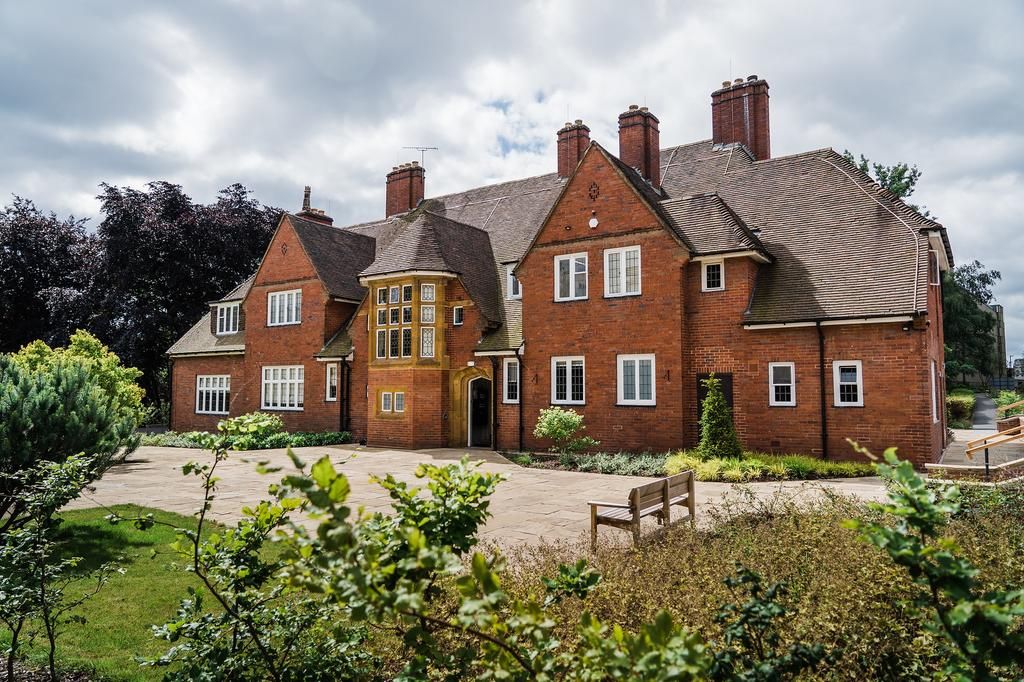 A large brick house with multiple chimneys, a central entrance, and a paved courtyard with a bench.