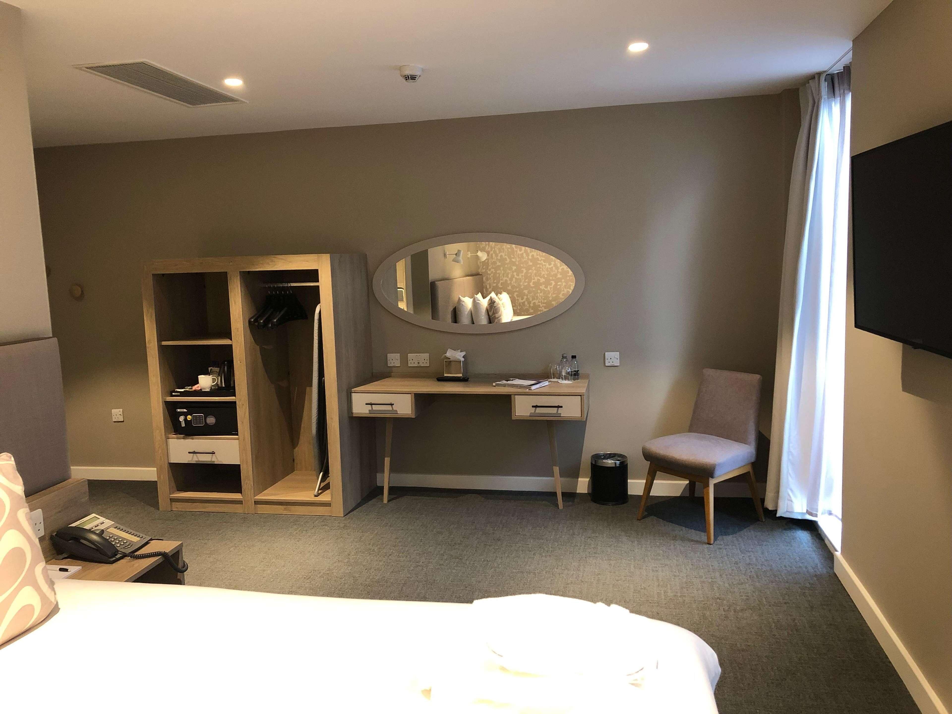 Habitación de hotel con cama, escritorio con espejo, silla, armario y televisor.