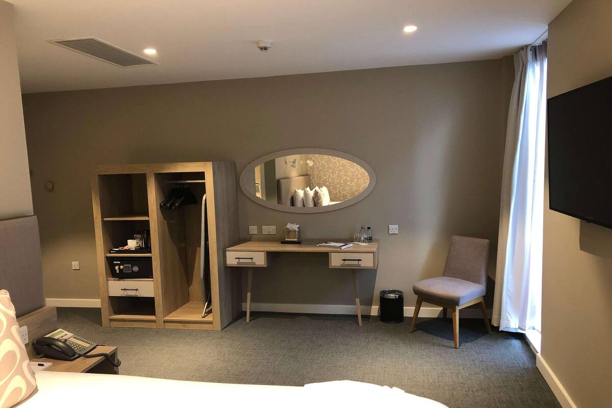 Habitación de hotel con cama, escritorio con espejo, silla, armario y televisor.