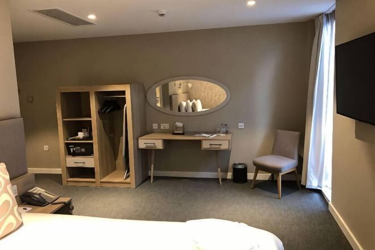 Habitación de hotel con cama, escritorio con espejo, armario, silla y televisor montado en la pared.