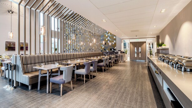 Un ristorante moderno con un lungo bancone, diverse aree salotto e una parete decorativa.