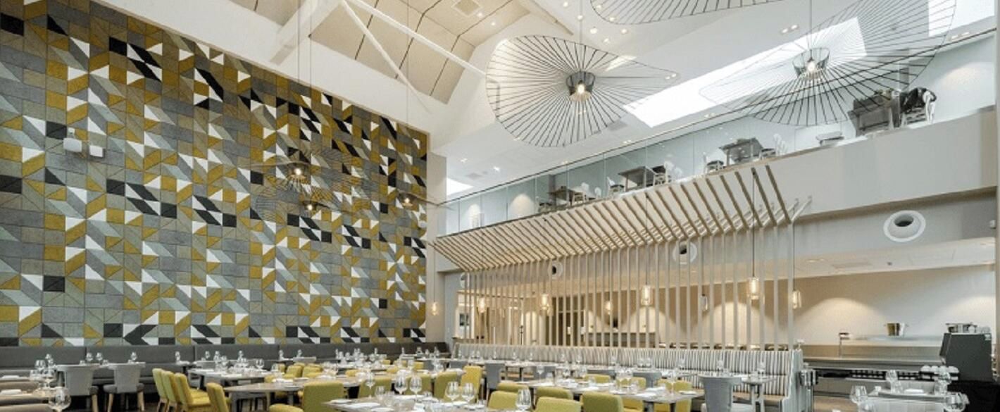 Un espace de restauration moderne avec des murs aux motifs géométriques, plusieurs tables et un plafond haut agrémenté de luminaires originaux.