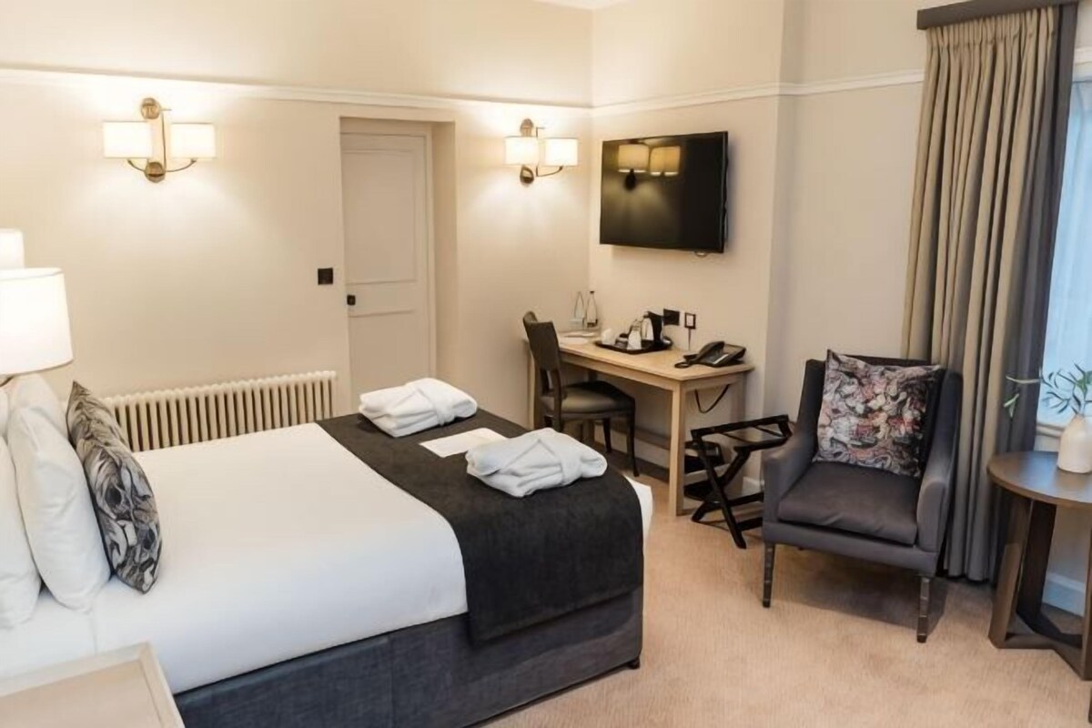 Habitación de hotel con cama, escritorio, silla, televisión y cortinas.