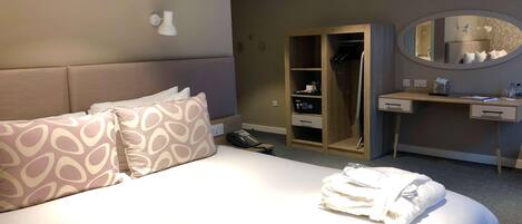 Habitación de hotel con cama, mesita de noche, espejo, armario y escritorio.