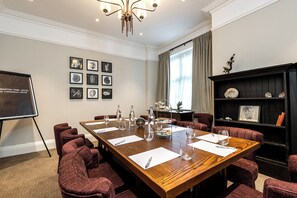 A conference room with a long wooden table, red upholstered chairs, a projector screen, framed pictures on the wall, and a bookshelf with decorative items. - Edgbaston Park Hotel & Conference Centre (Birmingham)